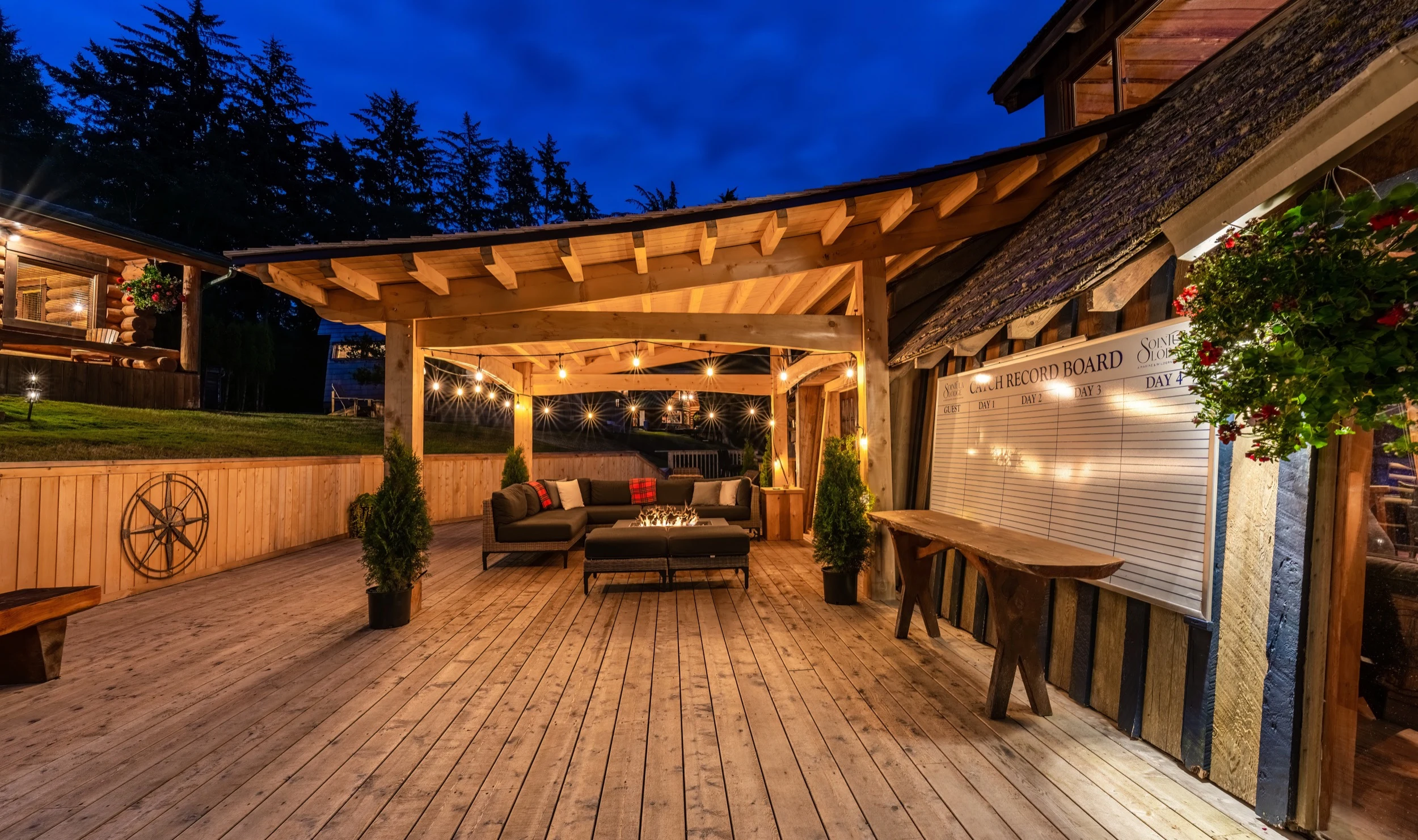 Sea Wolf Lodge outdoor lounge at night, fire pit glowing, string lights, BC wilderness