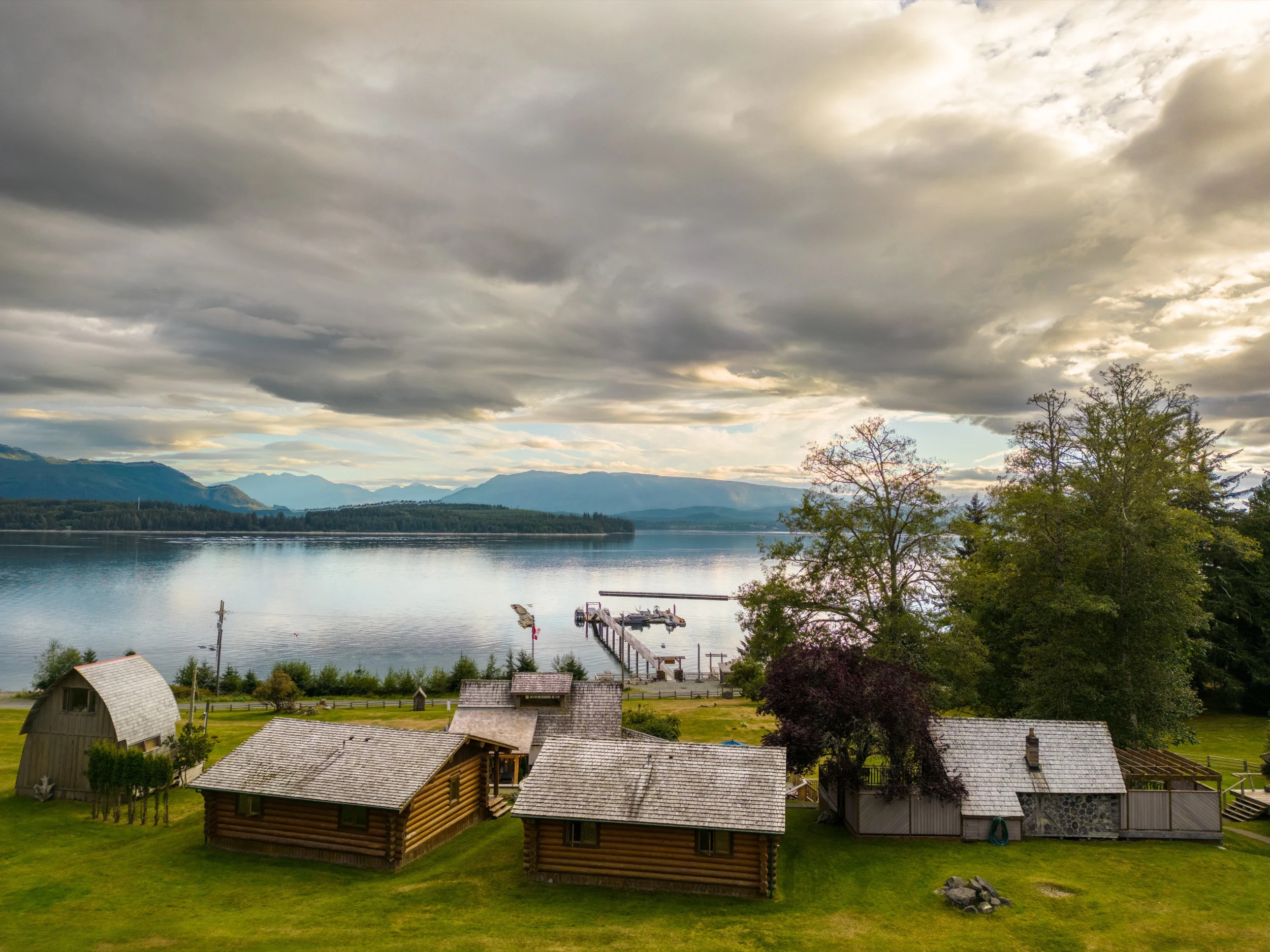 Aerial sunset view of Sea Wolf Lodge, multiple log cabins and main lodge on the BC coast, Kwakwaka'wakw Territory, Northern Vancouver Island